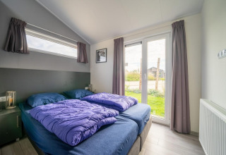 Chambre de lodge moderne avec lit double, couettes violettes et vue sur jardin, Hackfort 6, De Kraaijenbergse Plassen, Pays-Bas.