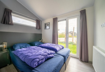 Modern lodge bedroom with double bed, purple duvets and garden view, Hackfort 6, De Kraaijenbergse Plassen, Netherlands.