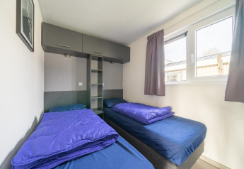 Bright twin room with blue bedding and large window at Hackfort 6 lodge, De Kraaijenbergse Plassen, Netherlands.