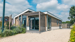 Moderne Hackfort 8 Lodge mit Holzverkleidung, großen Fenstern und Terrasse bei blauem Himmel.