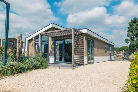 Moderne Hackfort 8 lodge met houtgevel, grote ramen, terras en blauwe lucht op de achtergrond.