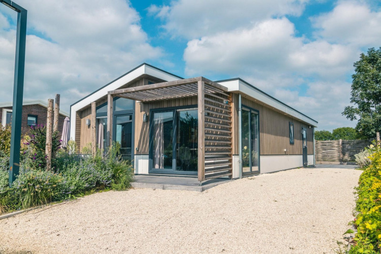 Lodge moderno Hackfort 8 con fachada de madera, grandes ventanales y terraza bajo un cielo azul.