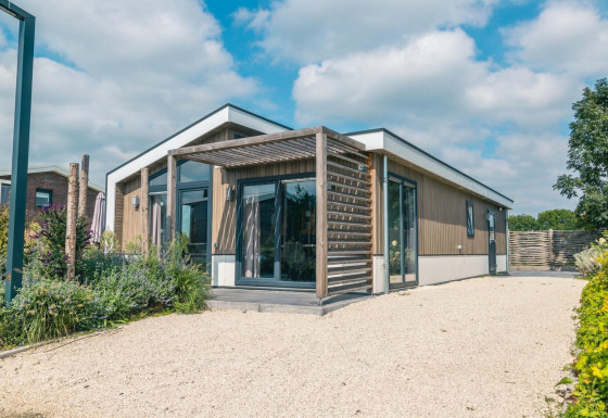 Moderne Hackfort 8 lodge met houtgevel, grote ramen, terras en blauwe lucht op de achtergrond.