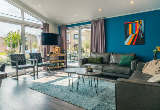Sala de estar moderna en la cabaña Hackfort 8 en De Kraaijenbergse Plassen, Países Bajos, con grandes ventanales.