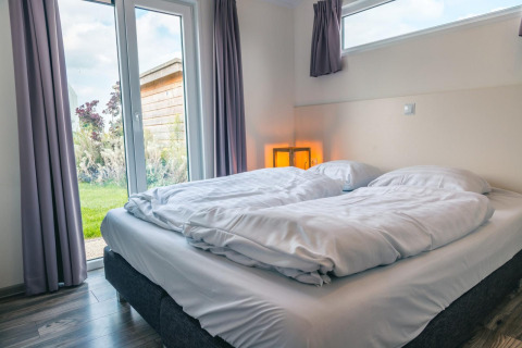 Chambre moderne au Hackfort 8, De Kraaijenbergse Plassen, Pays-Bas, lit double et vue sur le jardin extérieur.