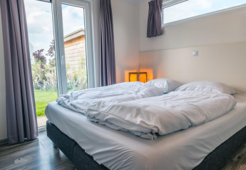 Chambre moderne au Hackfort 8, De Kraaijenbergse Plassen, Pays-Bas, lit double et vue sur le jardin extérieur.