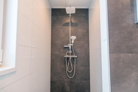 Moderne douche in Hackfort 8 lodge bij De Kraaijenbergse Plassen, Nederland, met zwarte wandtegels.