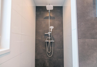 Moderne douche in Hackfort 8 lodge bij De Kraaijenbergse Plassen, Nederland, met zwarte wandtegels.