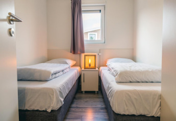 Habitación luminosa con dos camas individuales, mesita de noche y lámpara en Hackfort 8, De Kraaijenbergse Plassen.