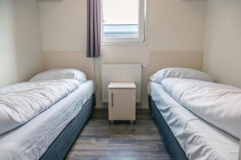 Chambre avec deux lits simples, linge de lit blanc et une table de nuit à Hackfort 8, De Kraaijenbergse Plassen.