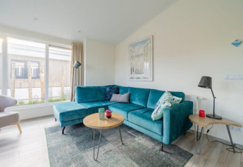 Lys stue med stor turkis sofa, moderne møbler og store vinduer i Hackfort Waterfront 4, Nederlandene.