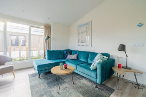 Lys stue med stor turkis sofa, moderne møbler og store vinduer i Hackfort Waterfront 4, Nederlandene.