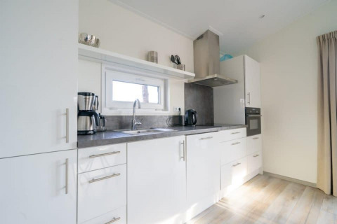 Cucina moderna con mobili bianchi, elettrodomestici in acciaio e piano grigio in un lodge olandese.