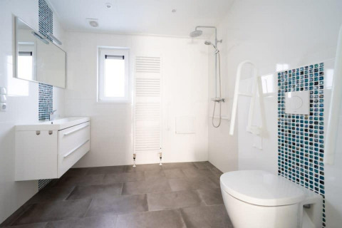 Modernes, barrierefreies Badezimmer in Hackfort Waterfront 4 mit Dusche, Haltegriffen und blauen Mosaikfliesen.