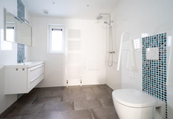 Moderne, rolstoeltoegankelijke badkamer in Hackfort Waterfront 4 met douche, steunen en blauwe mozaïektegels.