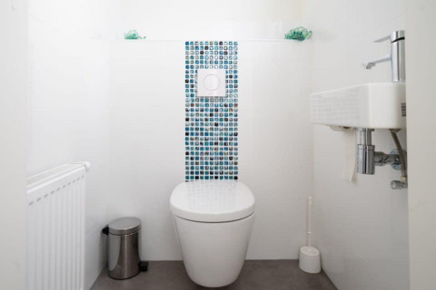 Baño moderno y minimalista con inodoro suspendido, lavabo pequeño y baldosas de mosaico en Hackfort Waterfront 4.