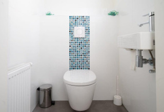 Baño moderno y minimalista con inodoro suspendido, lavabo pequeño y baldosas de mosaico en Hackfort Waterfront 4.