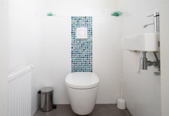Moderne, minimalistisk badeværelse med væghængt toilet, lille håndvask og mosaikfliser ved Hackfort Waterfront 4.
