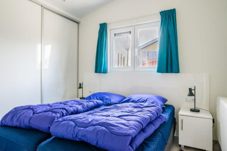 Bright bedroom at Hackfort Waterfront 4 lodge with blue bedding near De Kraaijenbergse Plassen, Netherlands.