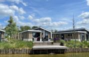 Moderne Hackfort Waterfront 6-lodges bij De Kraaijenbergse Plassen in Nederland, met blauwe lucht en wolken.