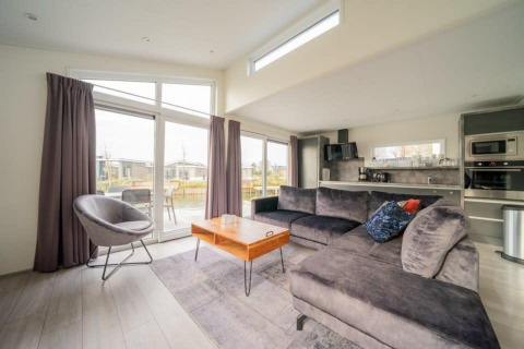 Salon moderne et lumineux au lodge Hackfort Waterfront 6 avec vue sur l’eau à De Kraaijenbergse Plassen, Pays-Bas.