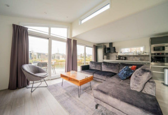 Salon moderne et lumineux au lodge Hackfort Waterfront 6 avec vue sur l’eau à De Kraaijenbergse Plassen, Pays-Bas.