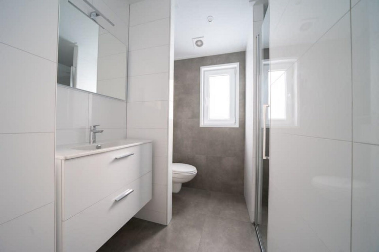 Baño moderno con muebles blancos, lavabo, espejo, inodoro y ventana en Hackfort Waterfront 6 en los Países Bajos.