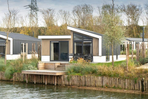 Lodge moderne Hackfort Waterfront 6 au bord de l’eau, De Kraaijenbergse Plassen, Pays-Bas, entouré de verdure.