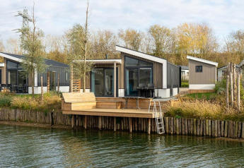 Moderne Hackfort Waterfront 8 lodge aan het water met breed terras, grote ramen en omringd door groen.