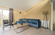 Sala moderna en la cabaña Hackfort Waterfront 8 con sofá azul, pared beige y grandes ventanales en Países Bajos.