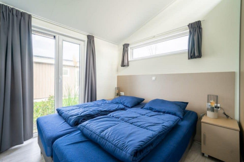 Dormitorio con dos camas individuales, ropa de cama azul y grandes ventanas en Hackfort Waterfront 8.