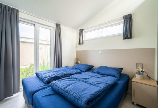 Dormitorio con dos camas individuales, ropa de cama azul y grandes ventanas en Hackfort Waterfront 8.