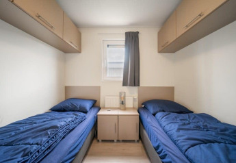 Twee eenpersoonsbedden met blauwe lakens in een sobere kamer in Hackfort Waterfront 8, Nederland.