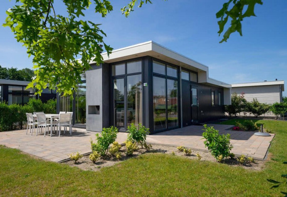 Modern Pavilion 6 lodge with large windows, patio dining area, and surrounding garden under clear blue sky.