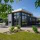 Moderne lodge Pavilion 6 med store vinduer, flisebelagt terrasse og udendørs spiseområde omgivet af grøn have.