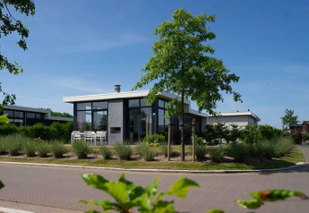 Alojamiento glamping moderno con grandes ventanales, terraza y vegetación abundante en día soleado.