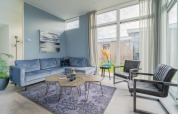 Stijlvolle loungehoek in een lodge met blauwe zetel, zwarte stoelen, grote ramen en moderne inrichting.