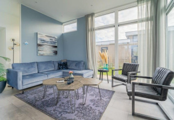 Stijlvolle loungehoek in een lodge met blauwe zetel, zwarte stoelen, grote ramen en moderne inrichting.