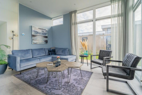 Salon moderne de lodge avec canapé bleu, deux fauteuils noirs, grandes fenêtres et décoration épurée.