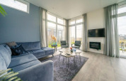 Moderne lodge-living met hoge ramen, blauwe hoekzetel, tv aan de muur en hedendaagse aankleding.