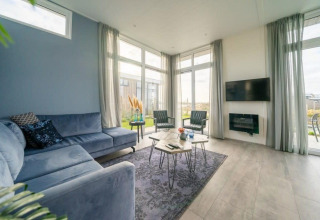 Modern lodge living room featuring large windows, a blue sectional sofa, wall-mounted TV, and decor.