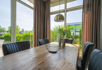 Luminoso comedor en una cabaña con sillas negras, mesa de madera, grandes ventanales y vista al jardín.
