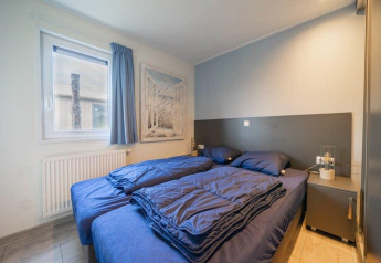Dormitorio moderno de lodge con dos camas individuales, ropa de cama azul oscuro, ventana y mesita.