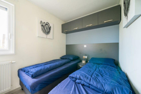 A bright lodge room with two single beds, blue bedding, overhead cabinets, and contemporary artwork.