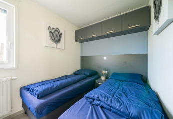 Lichte lodgekamer met twee aparte bedden, blauwe dekbedden, opbergkasten boven en moderne schilderijen.