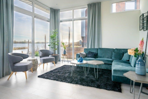 Moderne woonkamer met grote ramen, blauwe zetel en uitzicht op het water in Pavilion Waterfront 8, Nederland.