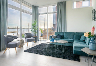 Salón moderno con grandes ventanales, sofá azul y vista al lago en Pavilion Waterfront 8, Países Bajos.