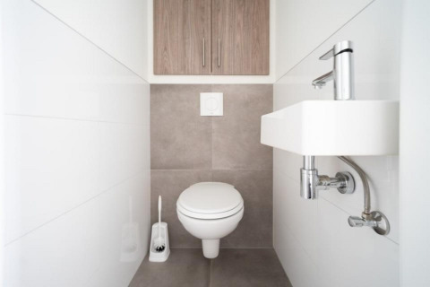 Moderne, minimalistische badkamer met hangtoilet, kleine lavabo en kast in Pavilion Waterfront 8, Nederland.