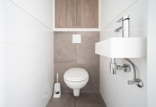 Moderne, minimalistische badkamer met hangtoilet, kleine lavabo en kast in Pavilion Waterfront 8, Nederland.