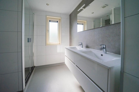 Moderne badkamer met dubbele lavabo, grote spiegel en douche in Pavilion Waterfront 8, Nederland.
